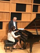 female student sits at piano while Julian Martin gives him instructions
