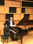 male student sits at piano while Julian Martin gives him instructions